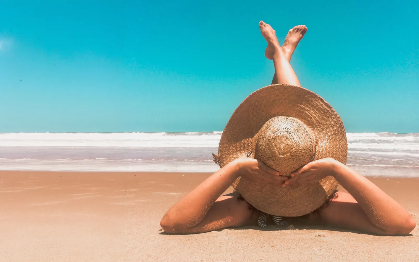 Person resting beneath a sun hat at the beach
